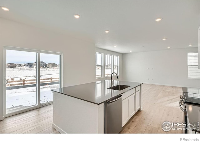 kitchen with a center island with sink, white cabinets, dark countertops, appliances with stainless steel finishes, and a sink