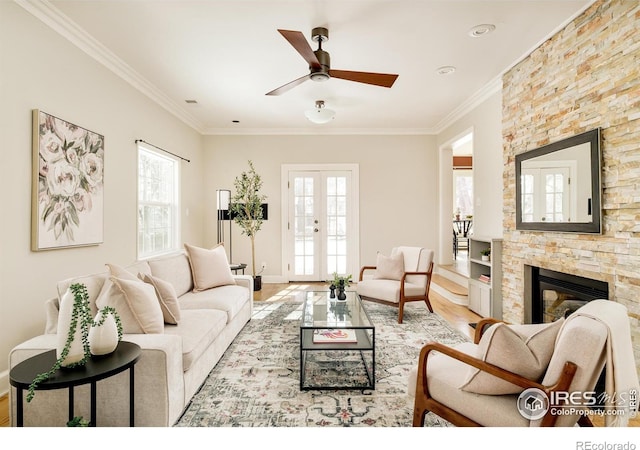 living area with a wealth of natural light, french doors, crown molding, and a stone fireplace