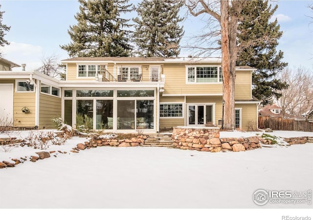 snow covered rear of property featuring a sunroom, fence, and a balcony