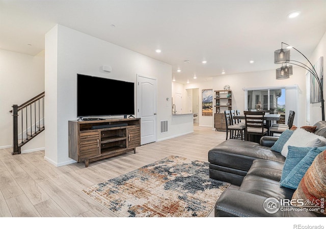 living area with light wood-type flooring, baseboards, recessed lighting, and stairs