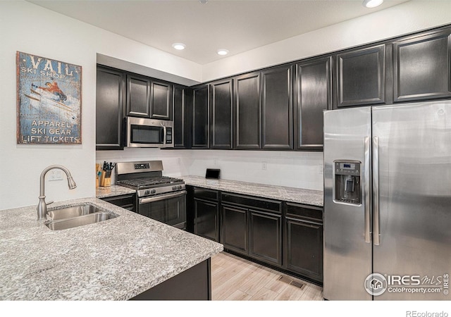 kitchen featuring appliances with stainless steel finishes, light wood-style floors, a sink, and light stone countertops