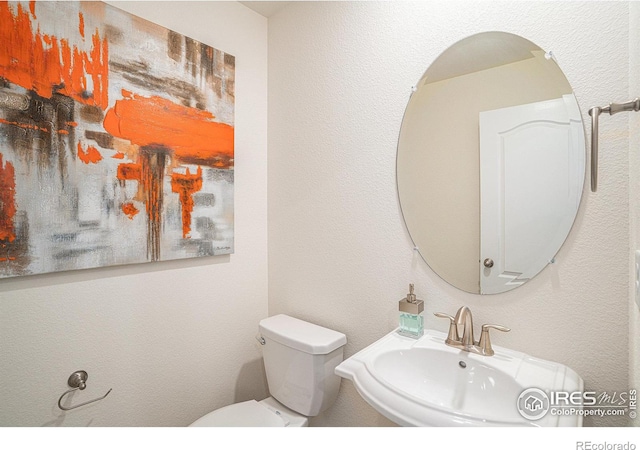 bathroom featuring a textured wall, a sink, and toilet