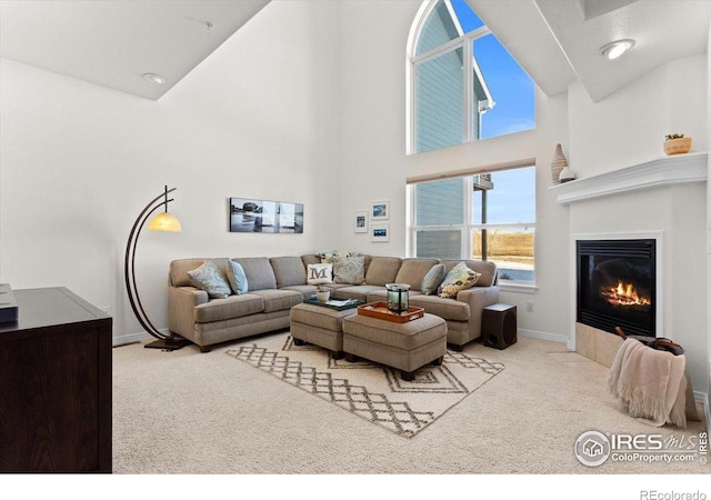 living area with baseboards, a high ceiling, a glass covered fireplace, and light colored carpet