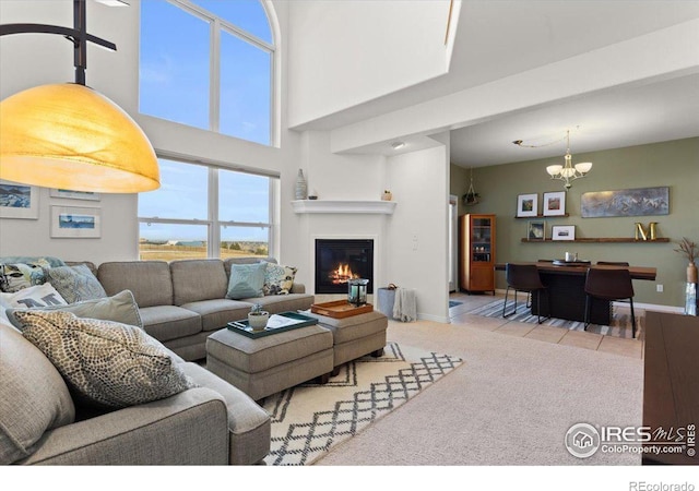 living area featuring light colored carpet, a towering ceiling, baseboards, a glass covered fireplace, and an inviting chandelier