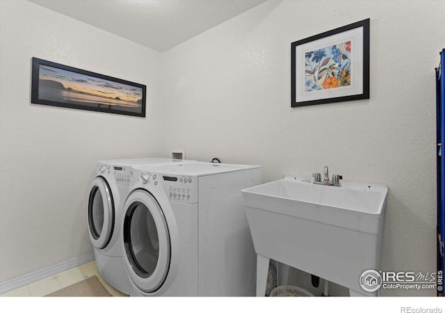 laundry room with a textured wall, laundry area, a sink, baseboards, and washing machine and clothes dryer