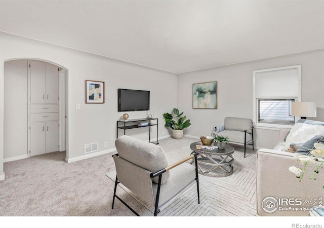 living area with light carpet, baseboards, visible vents, and arched walkways