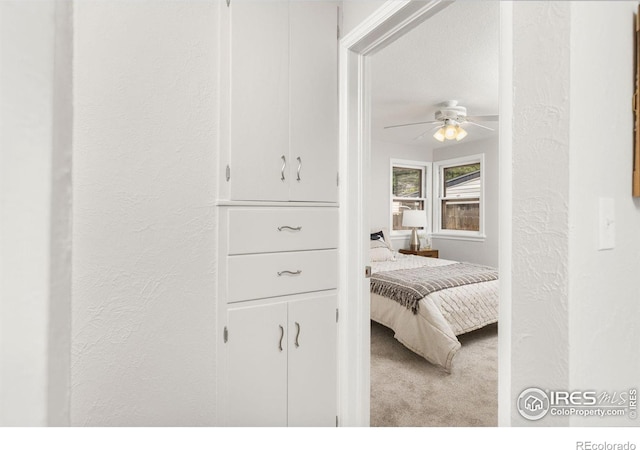 bedroom with a ceiling fan, light carpet, and a textured wall