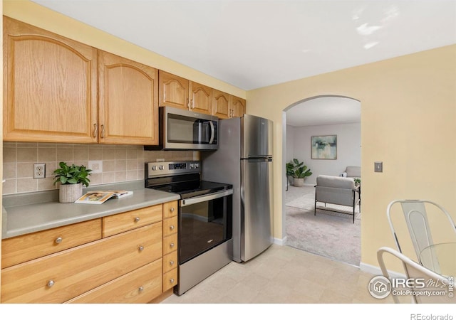 kitchen with arched walkways, light countertops, appliances with stainless steel finishes, light brown cabinetry, and tasteful backsplash