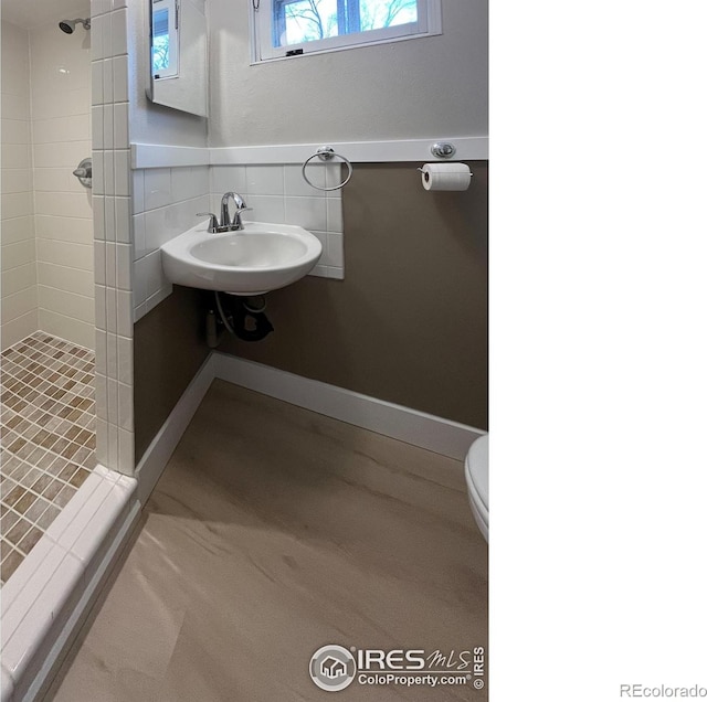 bathroom featuring tile walls, toilet, a sink, a shower stall, and baseboards