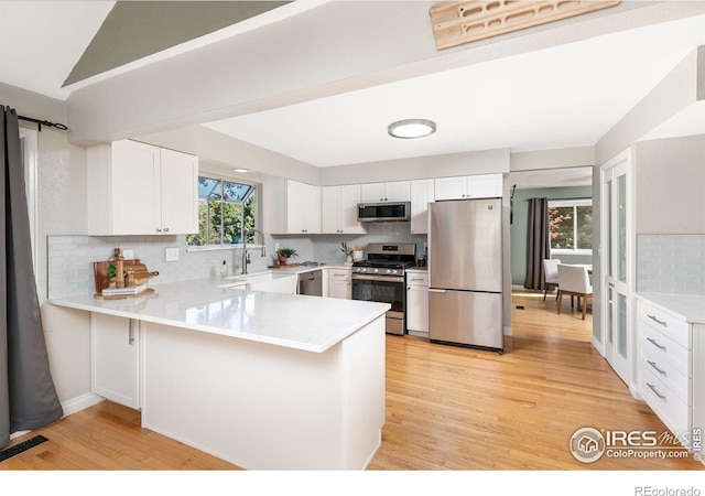 kitchen with a peninsula, white cabinets, stainless steel appliances, and light countertops