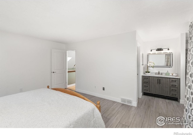 bedroom with connected bathroom, light wood-style flooring, a sink, visible vents, and baseboards