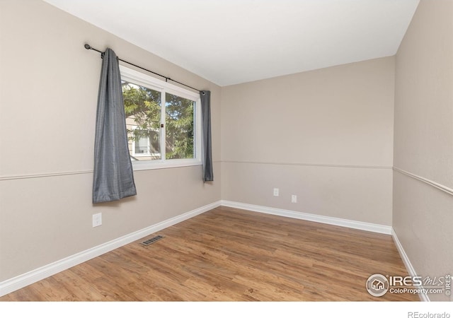 unfurnished room featuring wood finished floors, visible vents, and baseboards