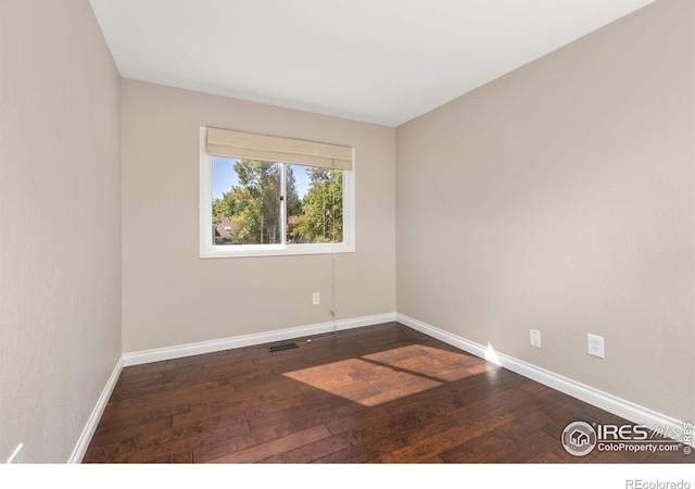 empty room featuring dark wood-style floors, visible vents, and baseboards