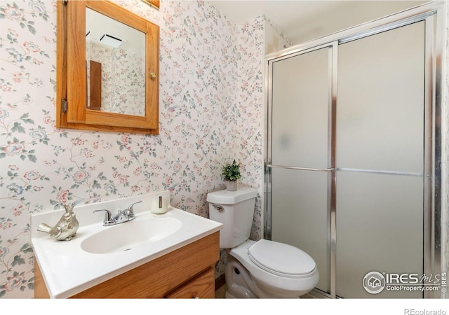 bathroom with a shower with shower door, vanity, toilet, and wallpapered walls