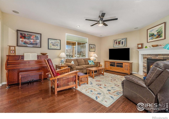 living area with dark wood-style floors, ceiling fan, and a stone fireplace