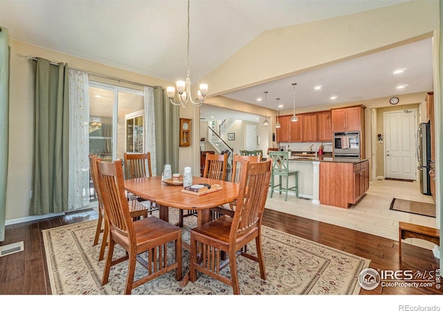 dining space with visible vents, lofted ceiling, light wood-style flooring, stairway, and an inviting chandelier