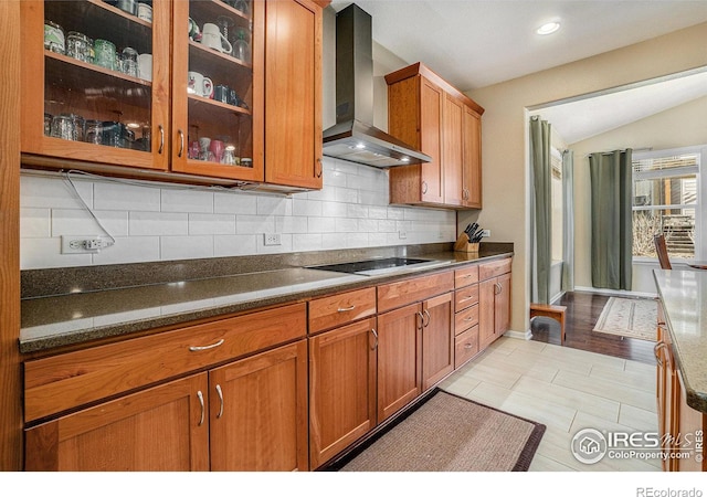 kitchen with wall chimney range hood, glass insert cabinets, and brown cabinets