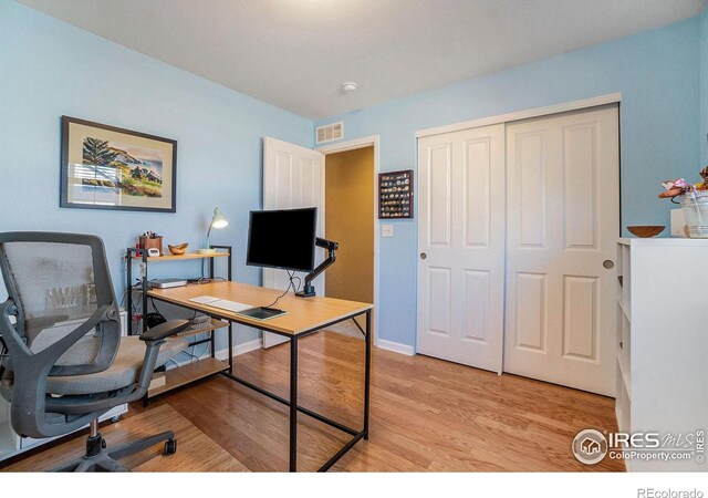 office area with light wood finished floors, visible vents, and baseboards