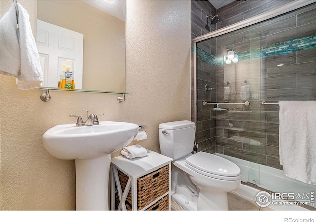 full bathroom with a stall shower, a sink, a textured wall, and toilet