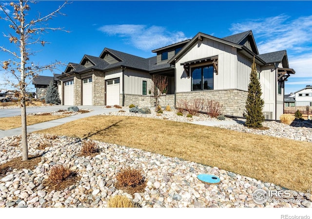 modern farmhouse with an attached garage, stone siding, driveway, and a front lawn