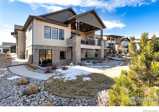 rear view of property with board and batten siding, stone siding, and a balcony