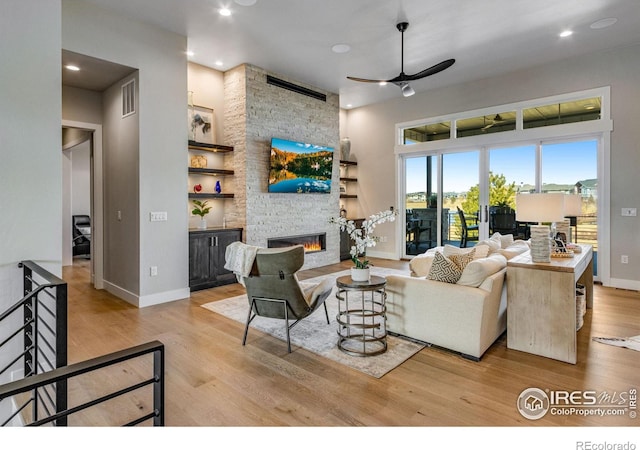 living area featuring visible vents, baseboards, ceiling fan, a stone fireplace, and light wood-type flooring