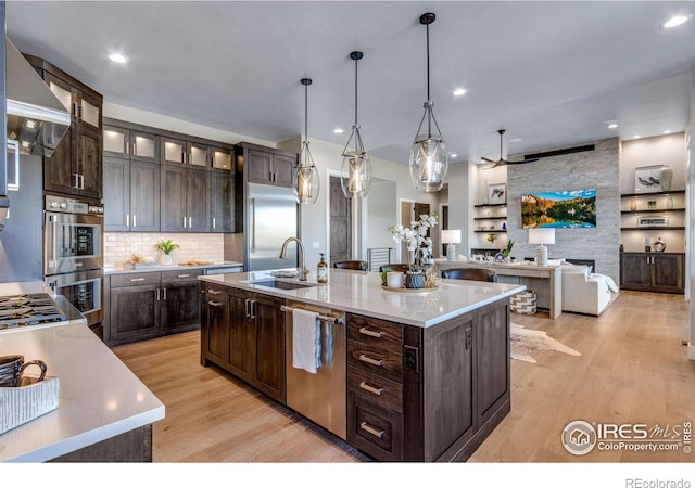 kitchen featuring a center island with sink, glass insert cabinets, appliances with stainless steel finishes, light countertops, and a sink