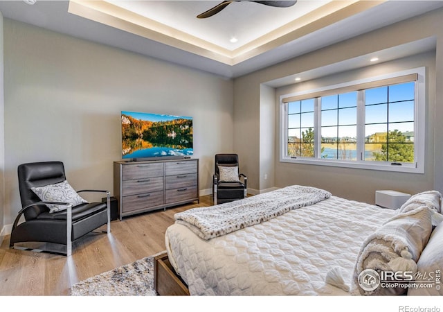 bedroom with a ceiling fan, a raised ceiling, baseboards, and light wood finished floors