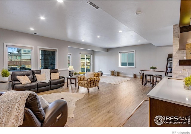 living room featuring baseboards, light wood-type flooring, visible vents, and recessed lighting