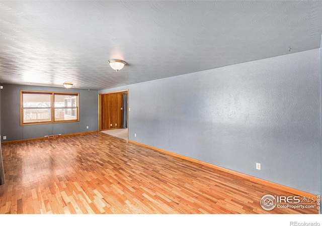 unfurnished room with wood finished floors, visible vents, and baseboards