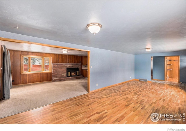 unfurnished living room featuring visible vents, wood walls, light wood-type flooring, a lit fireplace, and baseboards