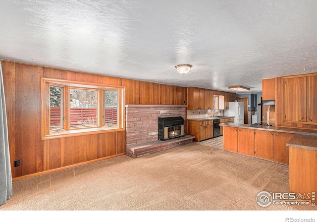 kitchen with wood walls, brown cabinetry, freestanding refrigerator, and light colored carpet