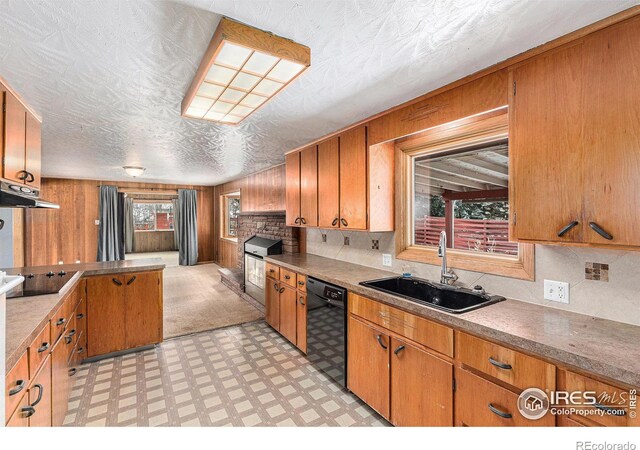 kitchen with light floors, wood walls, a sink, black appliances, and brown cabinetry