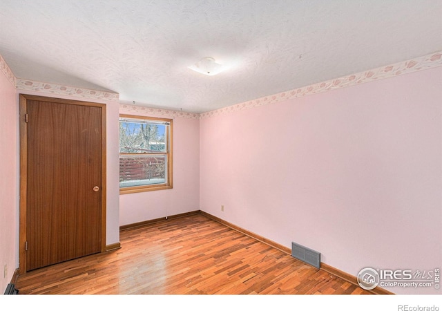 unfurnished bedroom featuring baseboards, light wood-style flooring, visible vents, and a textured ceiling