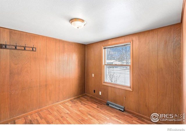 spare room with a textured ceiling, light wood finished floors, visible vents, and wooden walls