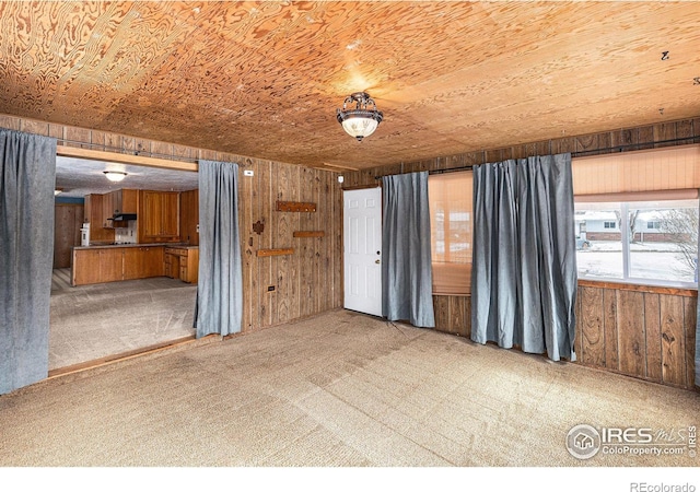 unfurnished living room with wooden ceiling, wood walls, and light carpet