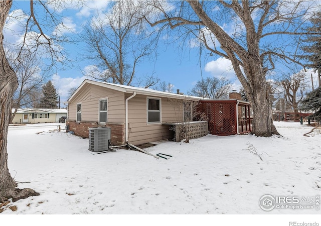 snow covered house with a chimney, central AC unit, and brick siding