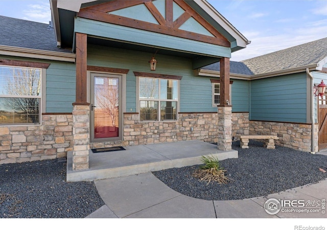 doorway to property with stone siding and a shingled roof