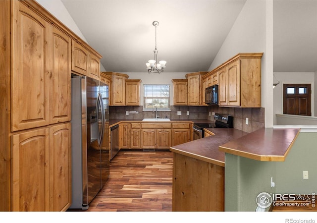 kitchen with dark countertops, appliances with stainless steel finishes, a peninsula, hanging light fixtures, and a sink