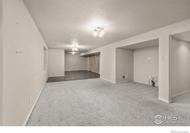 finished below grade area featuring a textured ceiling, carpet, visible vents, and baseboards