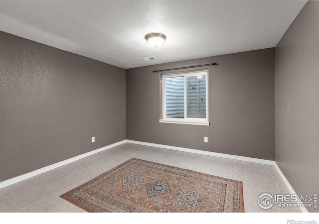 tiled spare room with a textured ceiling, visible vents, and baseboards