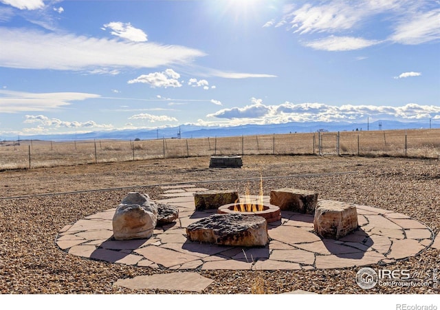 view of patio / terrace featuring a rural view, fence, a fire pit, and a mountain view