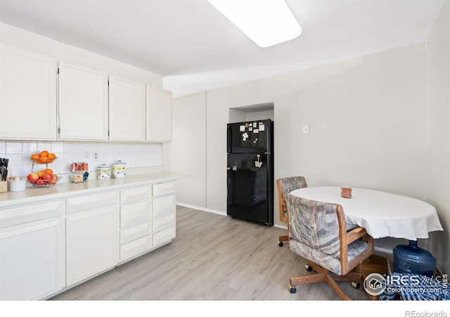 kitchen with light wood-type flooring, backsplash, freestanding refrigerator, and white cabinets