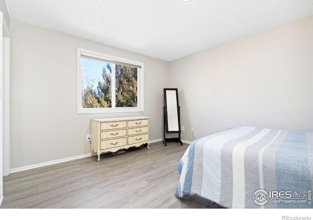 bedroom with a textured ceiling, light wood finished floors, and baseboards