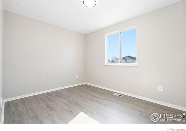 empty room featuring baseboards, visible vents, and wood finished floors