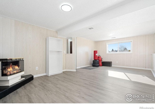 living area with a glass covered fireplace, a textured ceiling, baseboards, and wood finished floors