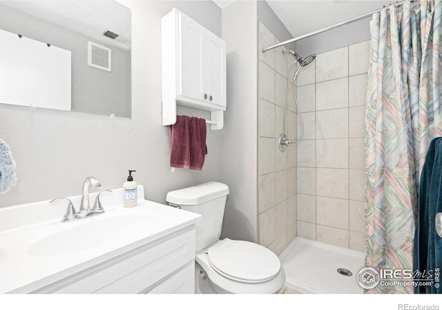 bathroom with toilet, tiled shower, vanity, and visible vents