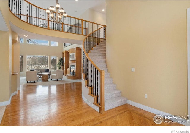 foyer entrance with baseboards, a glass covered fireplace, light wood-style flooring, stairs, and a notable chandelier