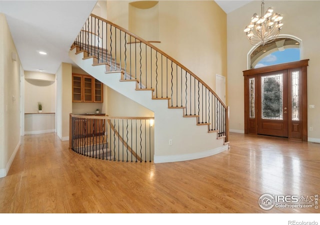 entryway with baseboards, light wood-style flooring, stairway, an inviting chandelier, and a high ceiling