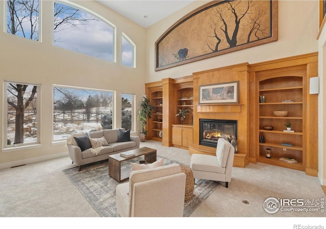 living room featuring a towering ceiling, a glass covered fireplace, visible vents, and light colored carpet